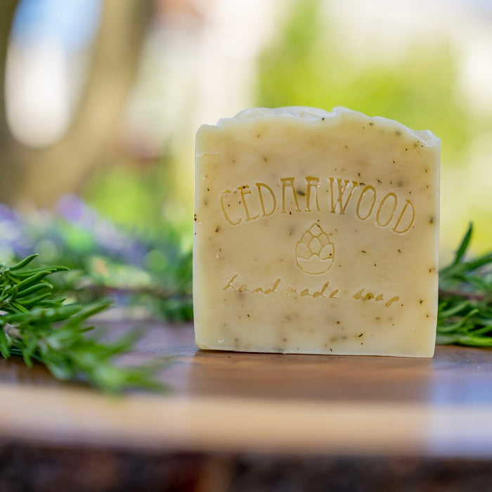 Bar of rosemary soap on a wooden surface with greenery in the background