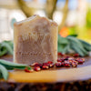 Bar of sandalwood soap on a wooden surface with greenery in the background