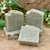 Three bars of French green clay soap on a wooden surface with greenery in the background