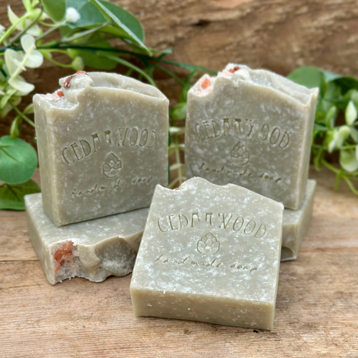 Three bars of French green clay soap on a wooden surface with greenery in the background