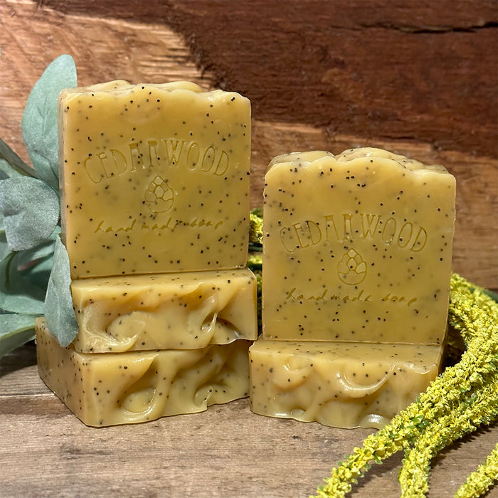 Three bars of lemon poppy seed soap on a wooden surface with greenery.