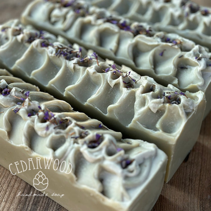 Bar of soap with lavender petals on a wooden surface, branded 'Cedarwood'.